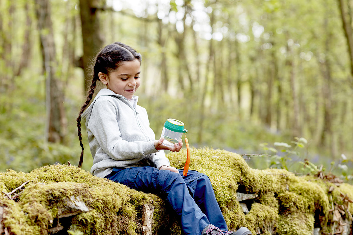 A young girl learning about nature with an insect observation jar - one of the key benefits of outdoor play in early years