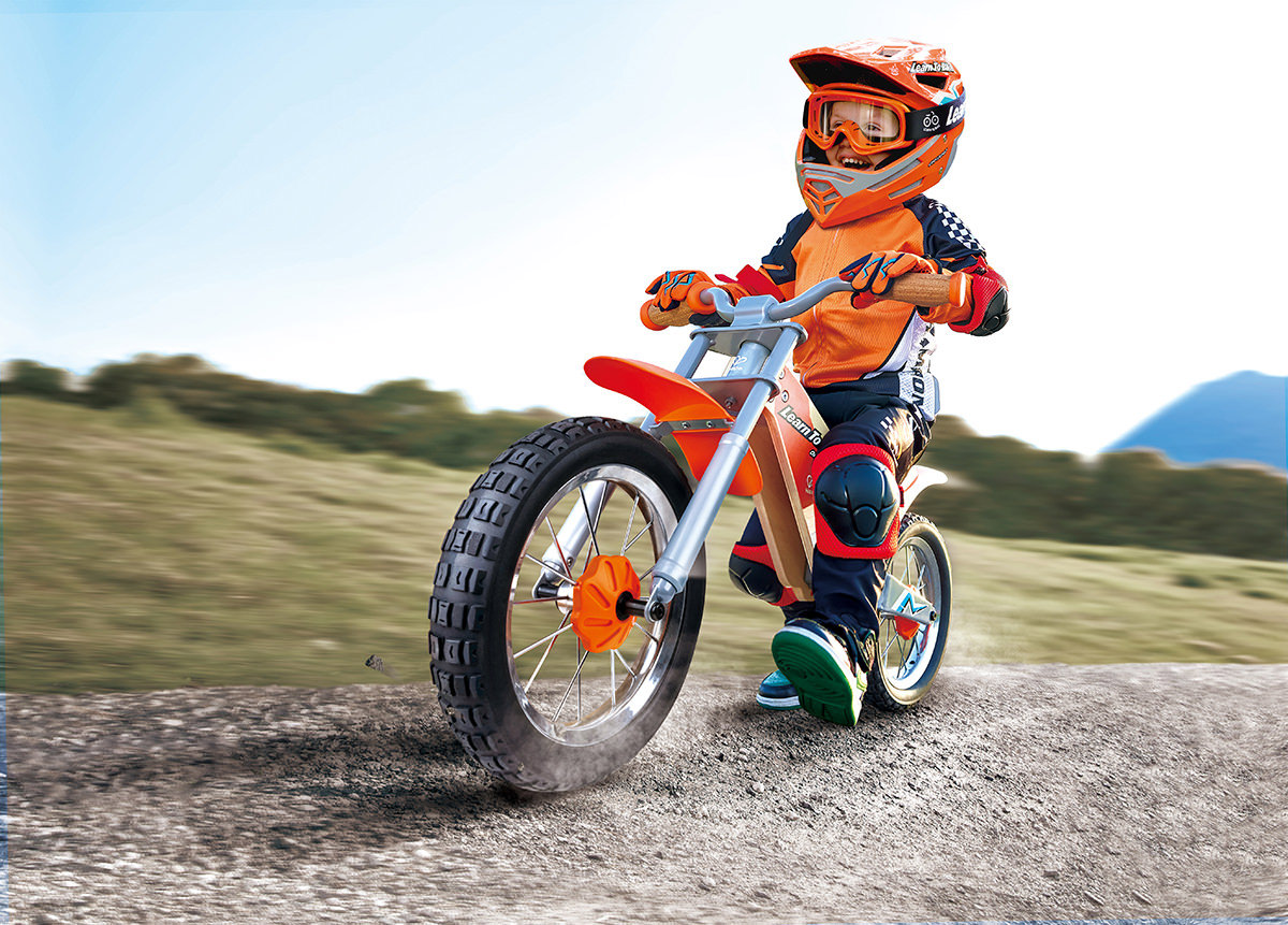 Child wearing safety gear riding an off-road balance bike on a dirt path – one of the best toys for outside play that builds strength, balance and confidence.