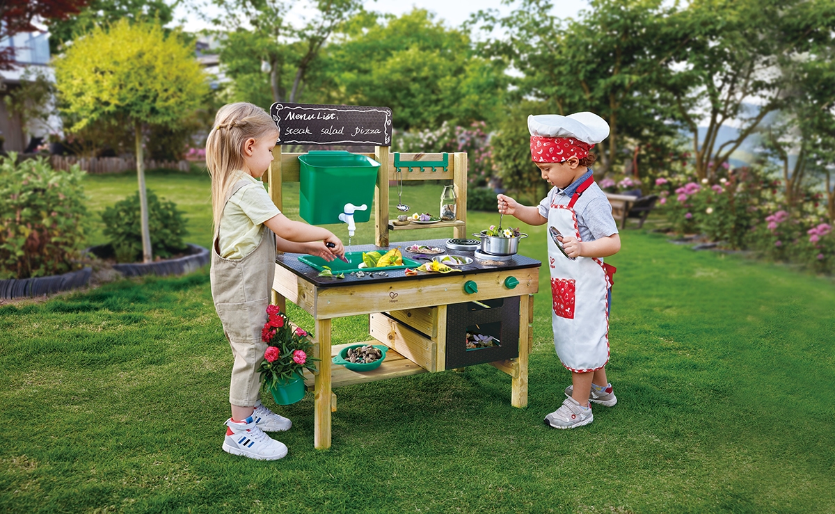 Two children play chef with the Outdoor Kitchen in a sunny garden, enjoying imaginative, messy outdoor play.