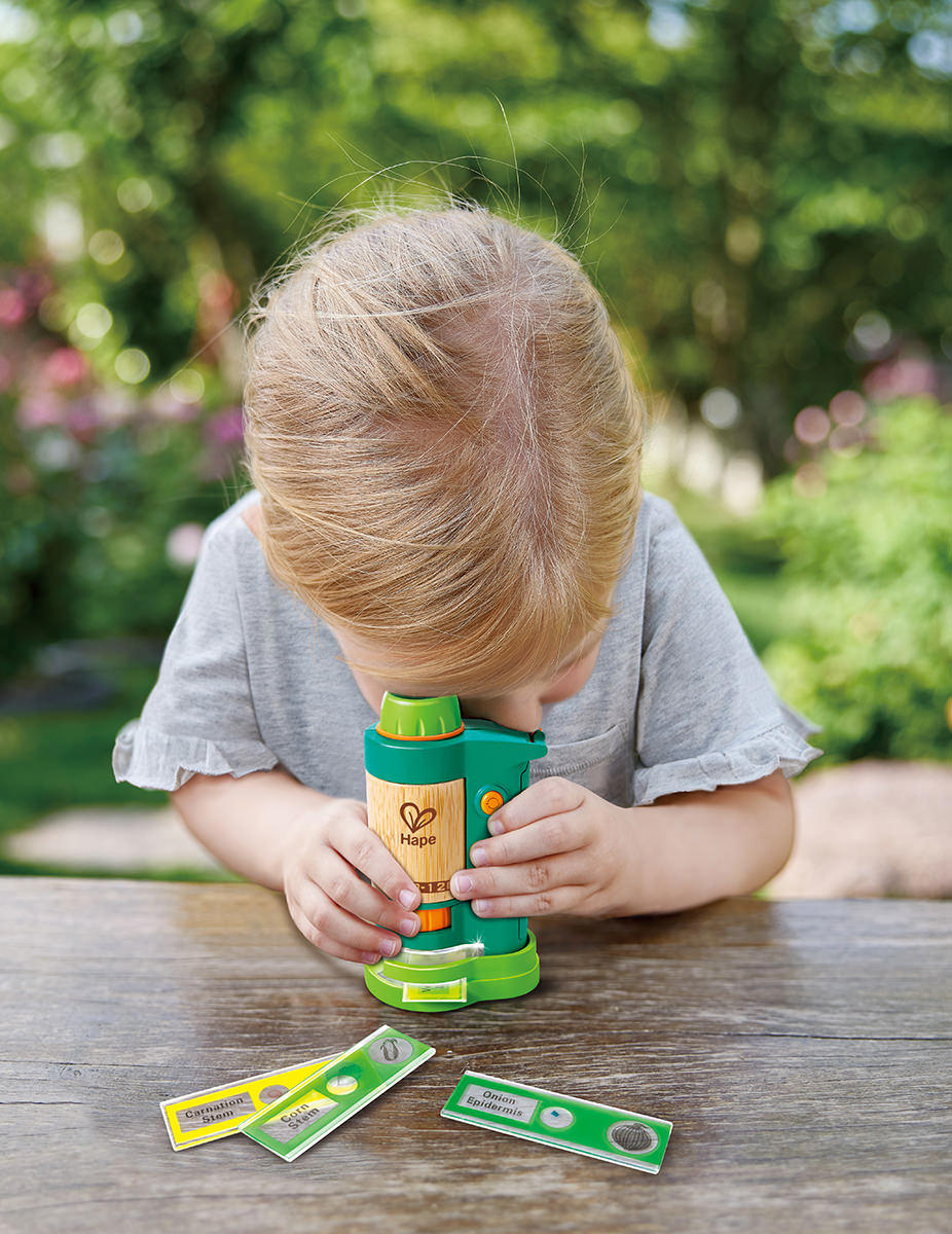 Young girl using a field microscope to study plant slides outdoors – a brilliant STEM toy for outside play that sparks curiosity and scientific discovery.